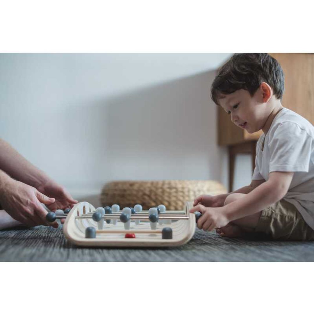 kid playing with a wood soccer game by Plan Toys