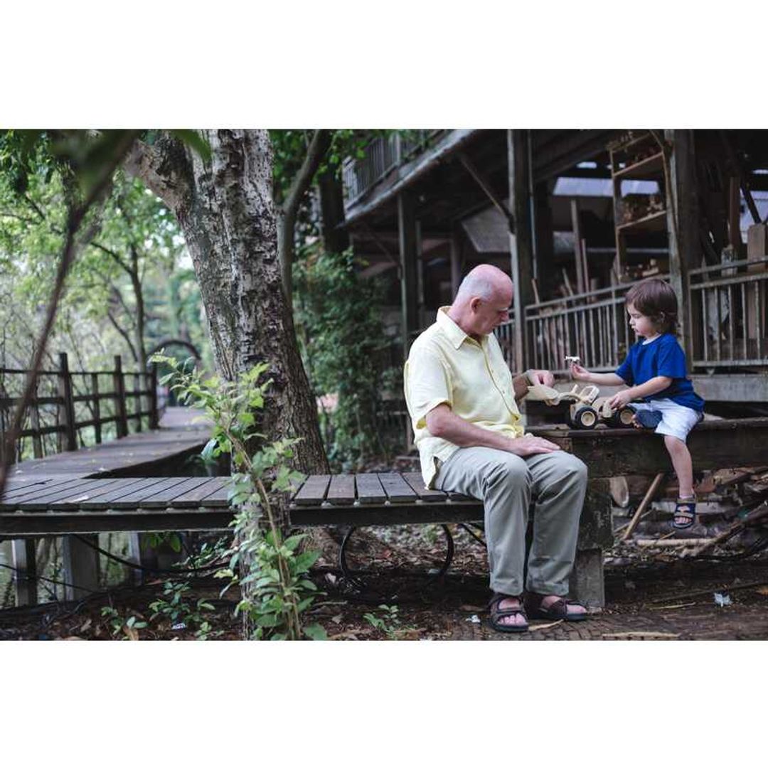 Grandparent and child outside stilling on a bench with aBulldozer by Plan Toys