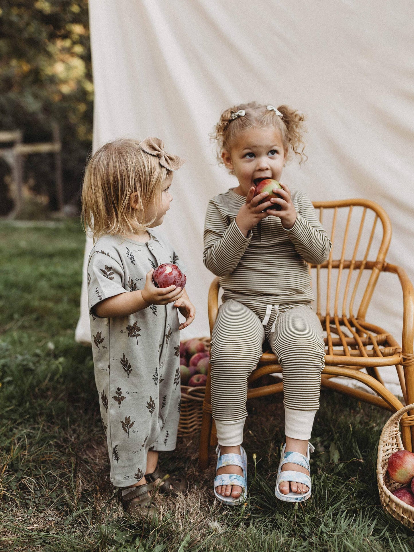 two children sitting outside eating apples wearing outfits by Ziwi Baby