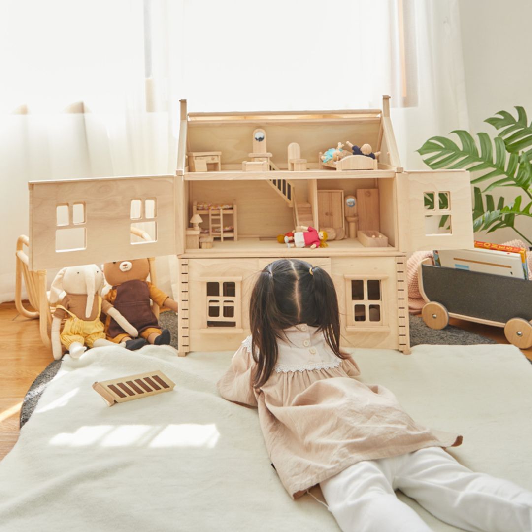 Child playing with a Victorian Dollhouse by Plan Toys