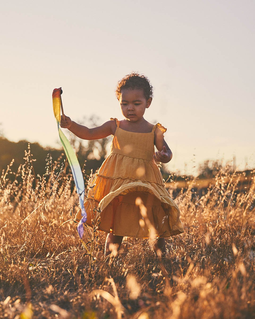 child walking in a field playing with mini rainbow silk streamer