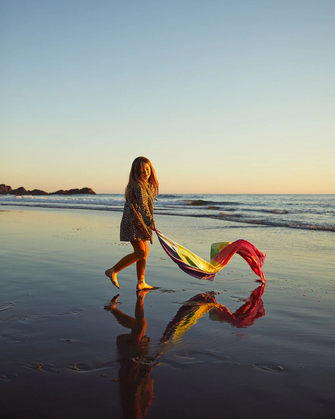 Child playing at the beach with a large rainbow play silk. The gentle waves are in the back ground