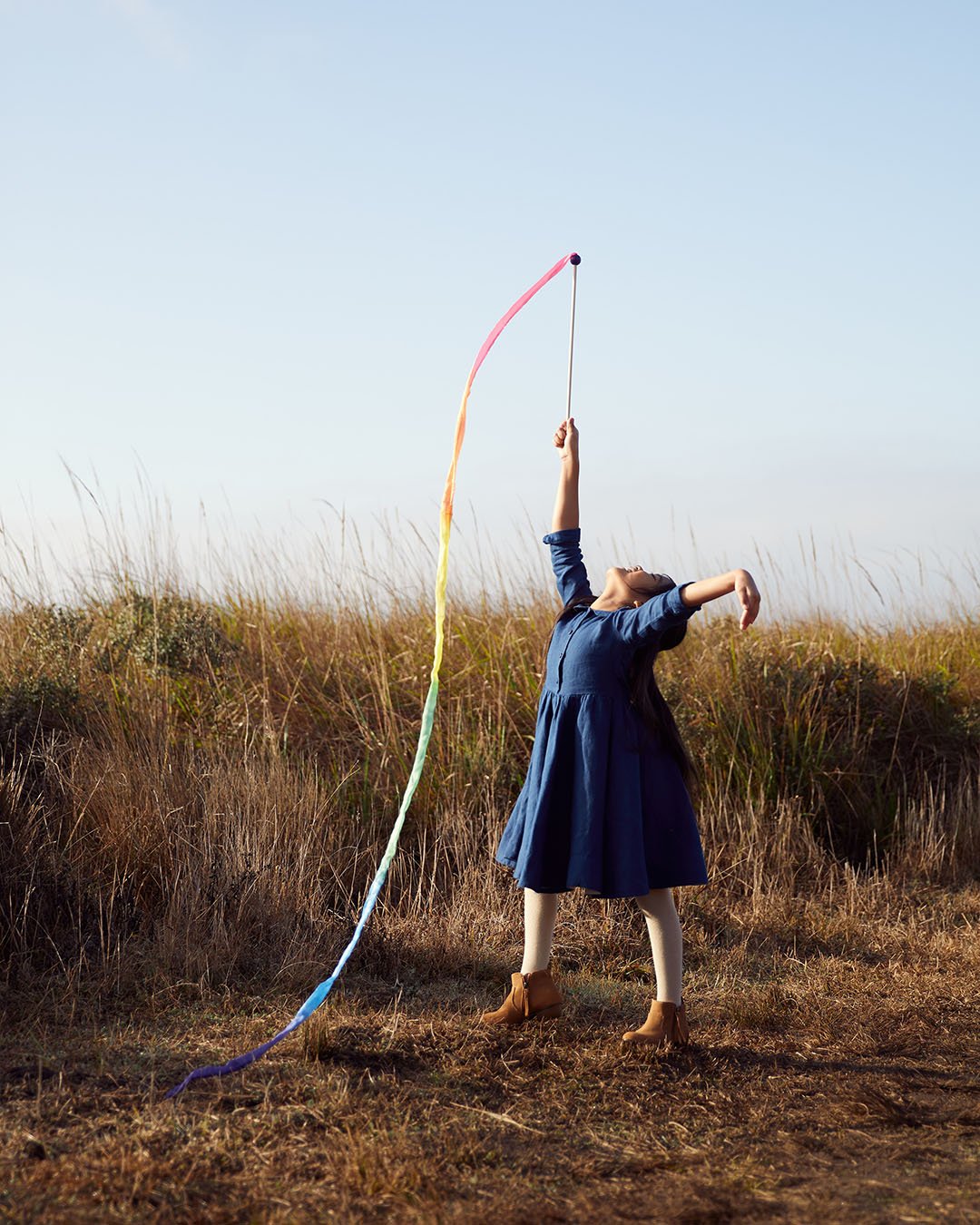 Child standing in a field playing with rainbow silk streamer