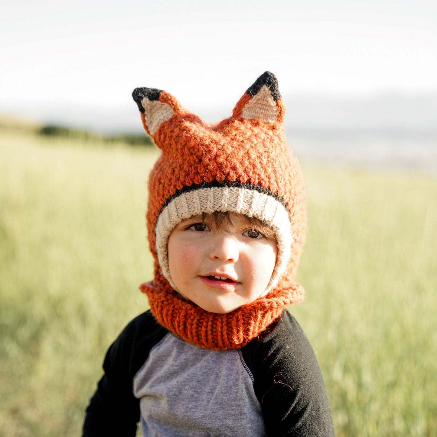 Child standing in a field wearing Fox animal hood by andes gifts