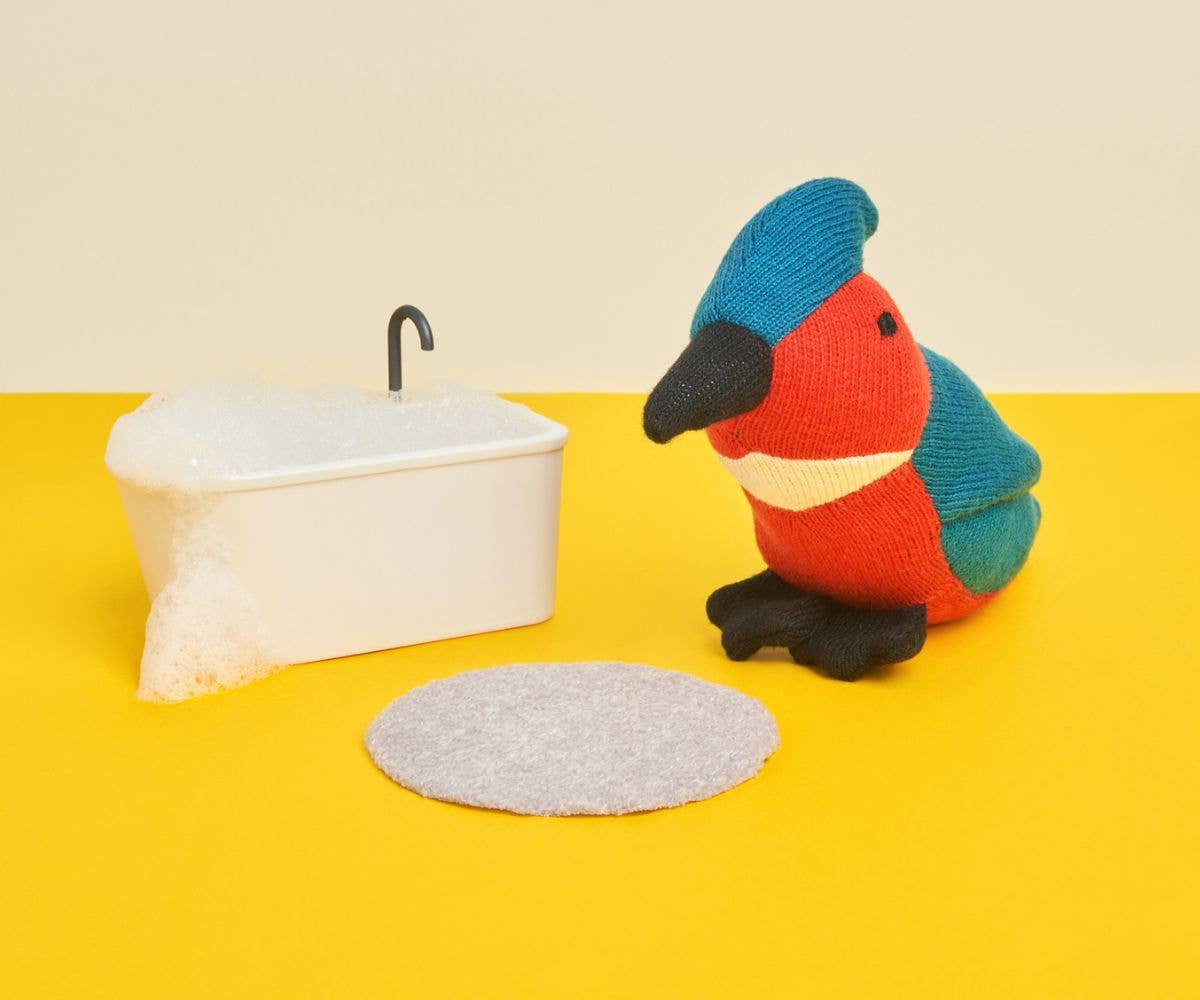 Organic kingfisher plush toy sitting next to a little plastic tub