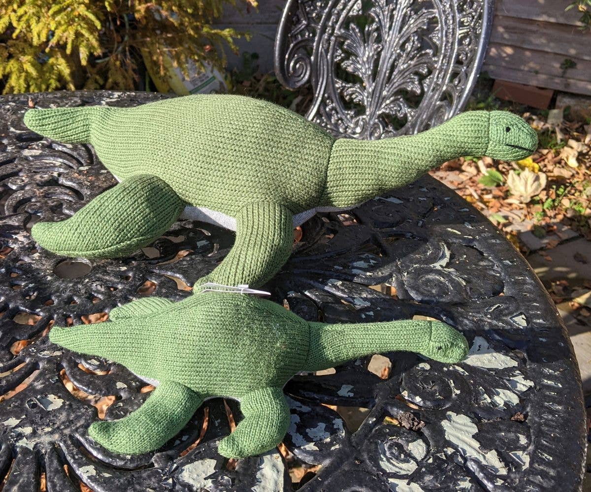 Two green knitted plesiosaurus plush toys on a cast iron table