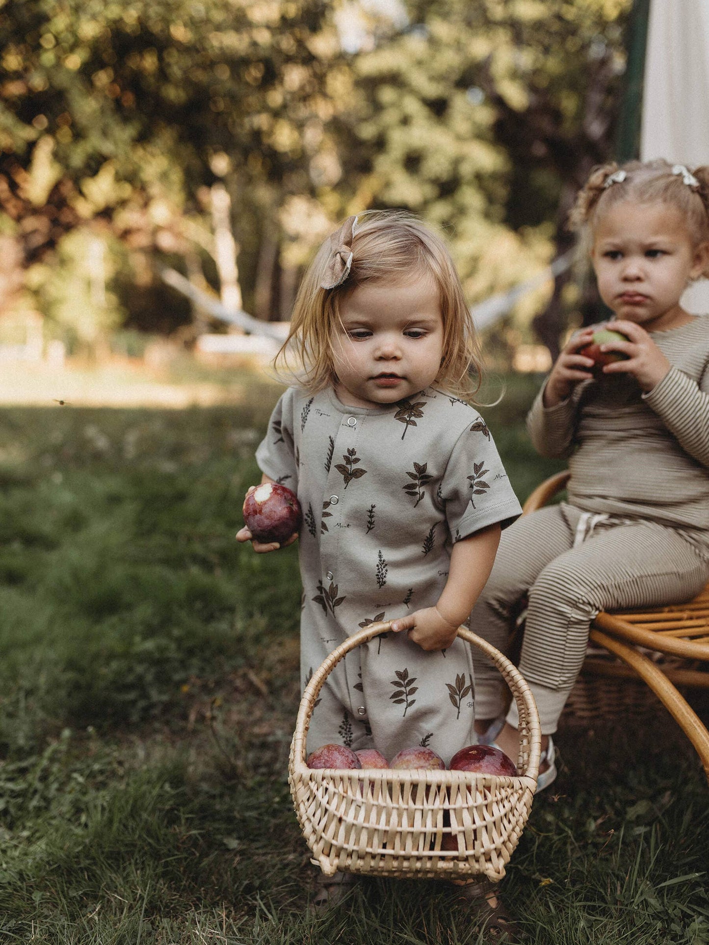 child holding an basket full of apples wearing herb organic summer romper