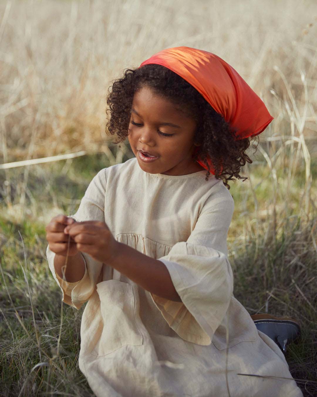 child sitting in a field wearing a fire mini playsilk as a bandana