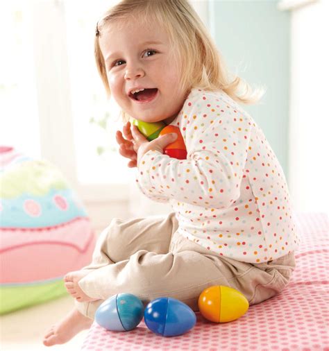 a child sitting on a bed wearing a polka dot shirt and brown pants holding haba musical eggs