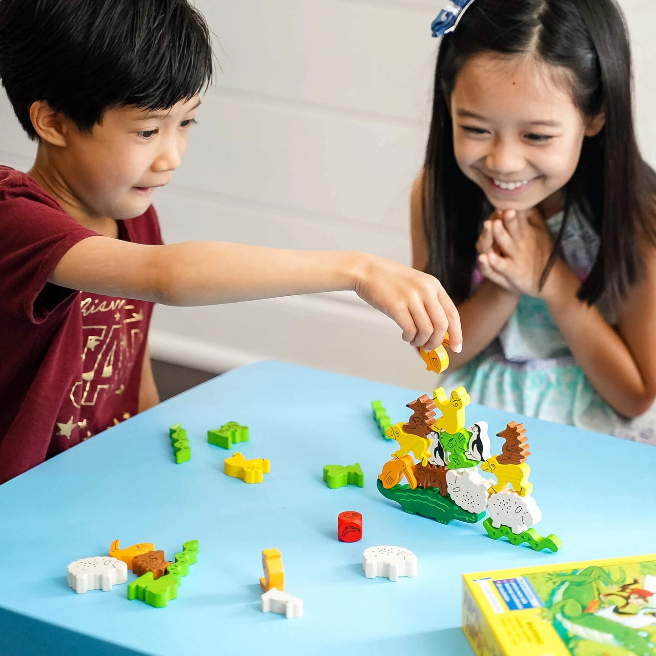 two children playing animal upon animal game on a blue table