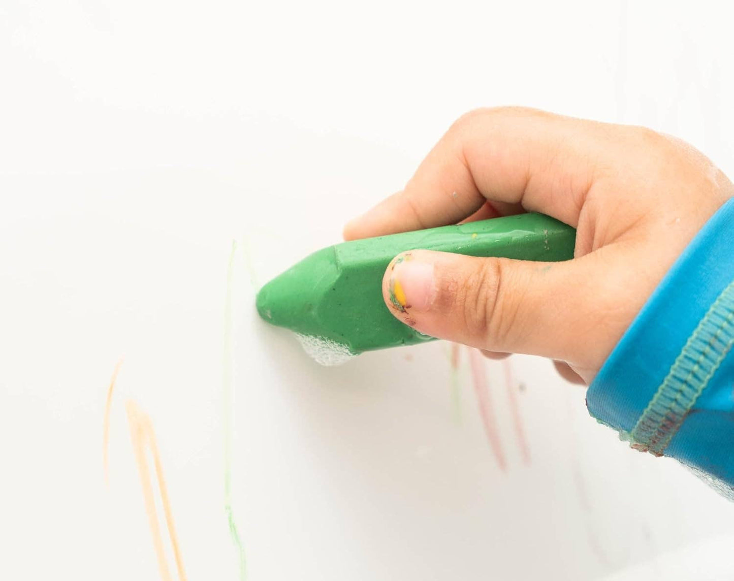 a child's hand holding a green triangle bath crayon drawing on the side of a bathtub