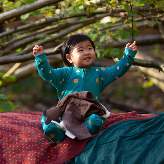 baby sitting on a blanket outside wearing a turquoise skies zip footies