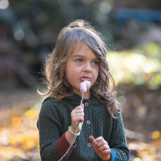 Child standing outside eating a s'more on a stick wearing a green hooded cardigan