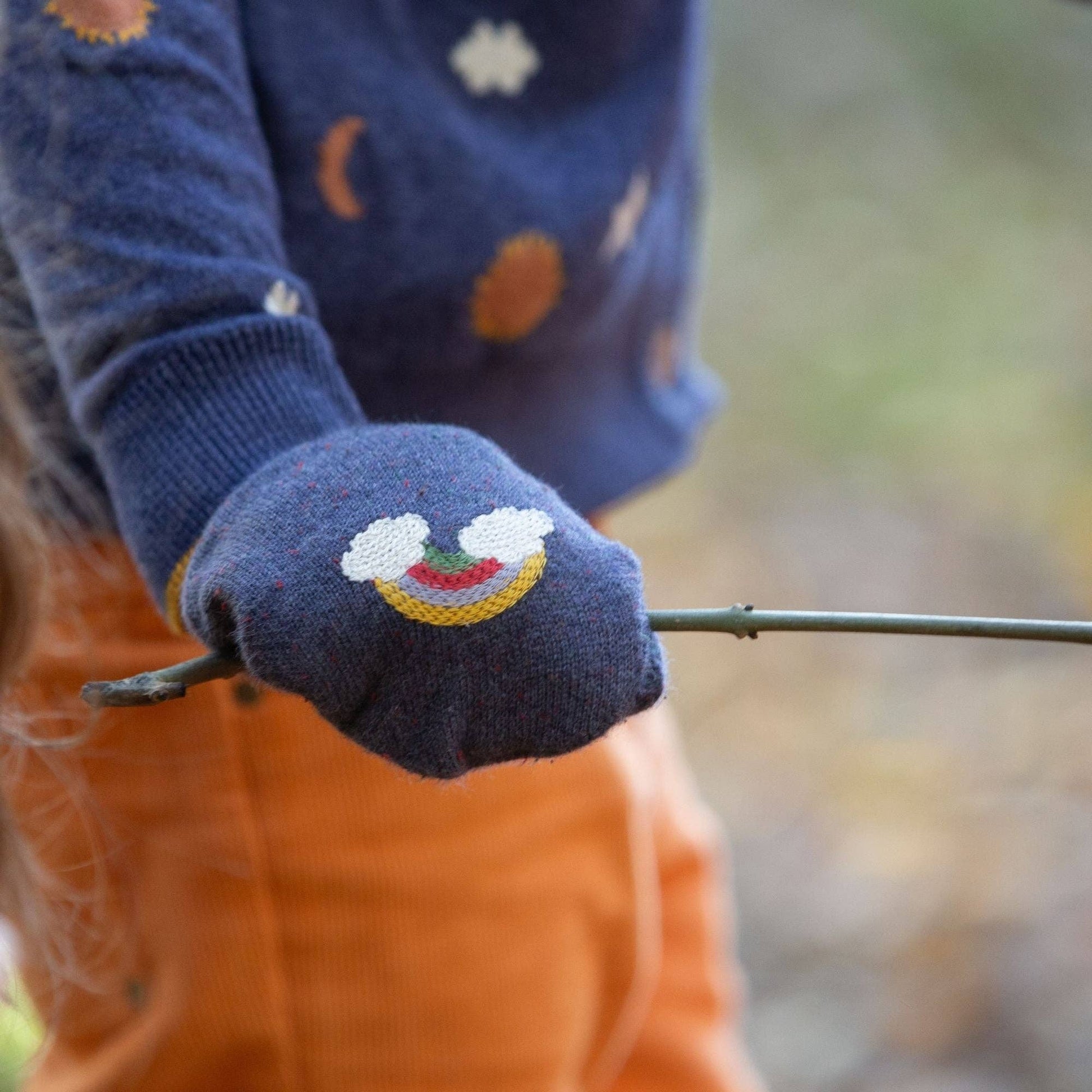 close-up of a child's hand holding a stick and wearing blue knitted rainbow mitten