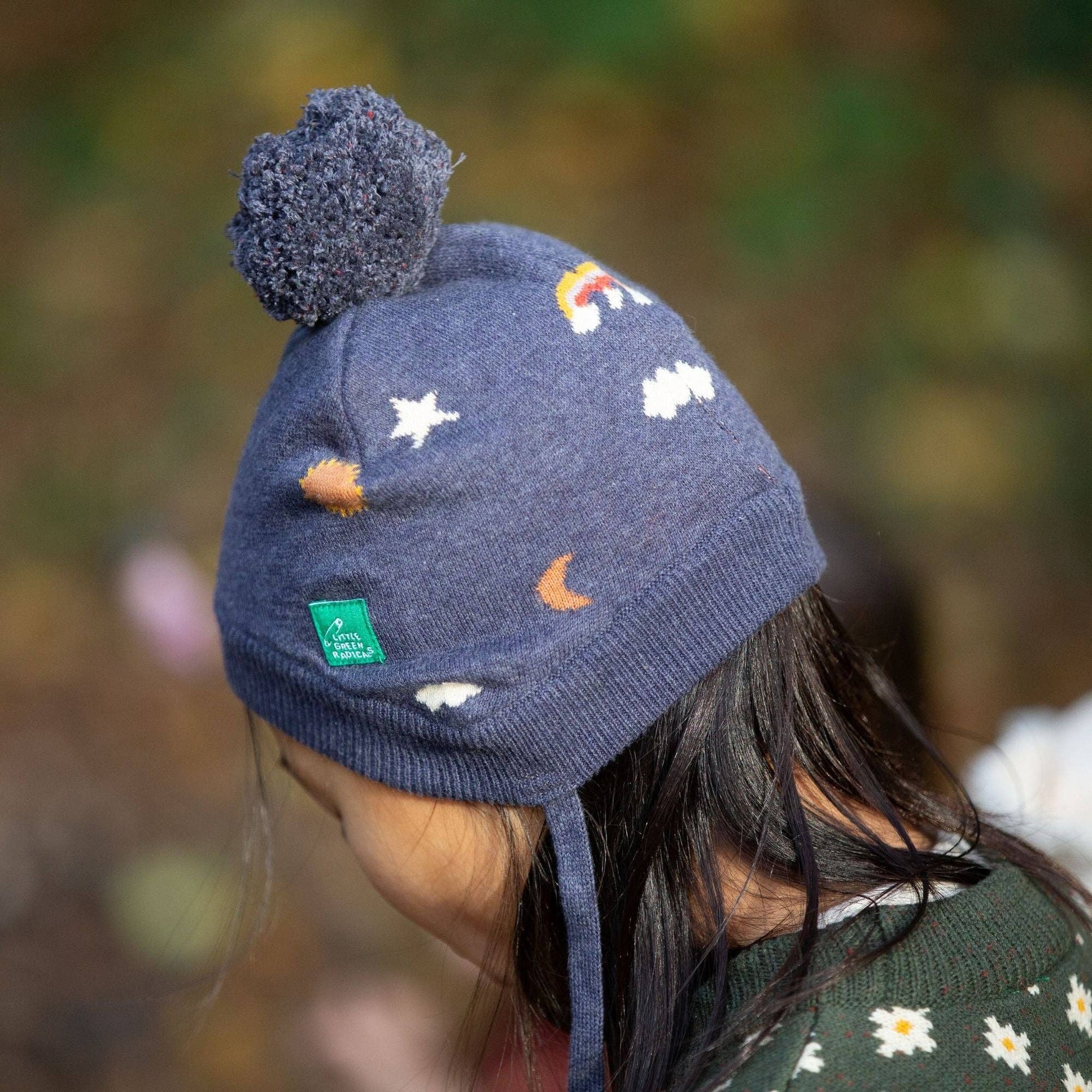 child standing outside wearing around the sun knitted hat