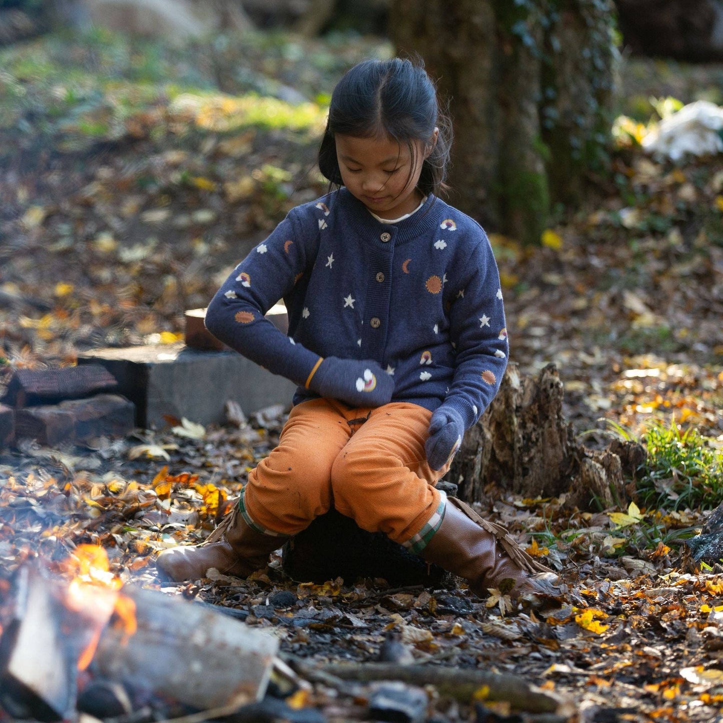 Child sitting outdoors around a fire wearing an around the sun knitted cardigan