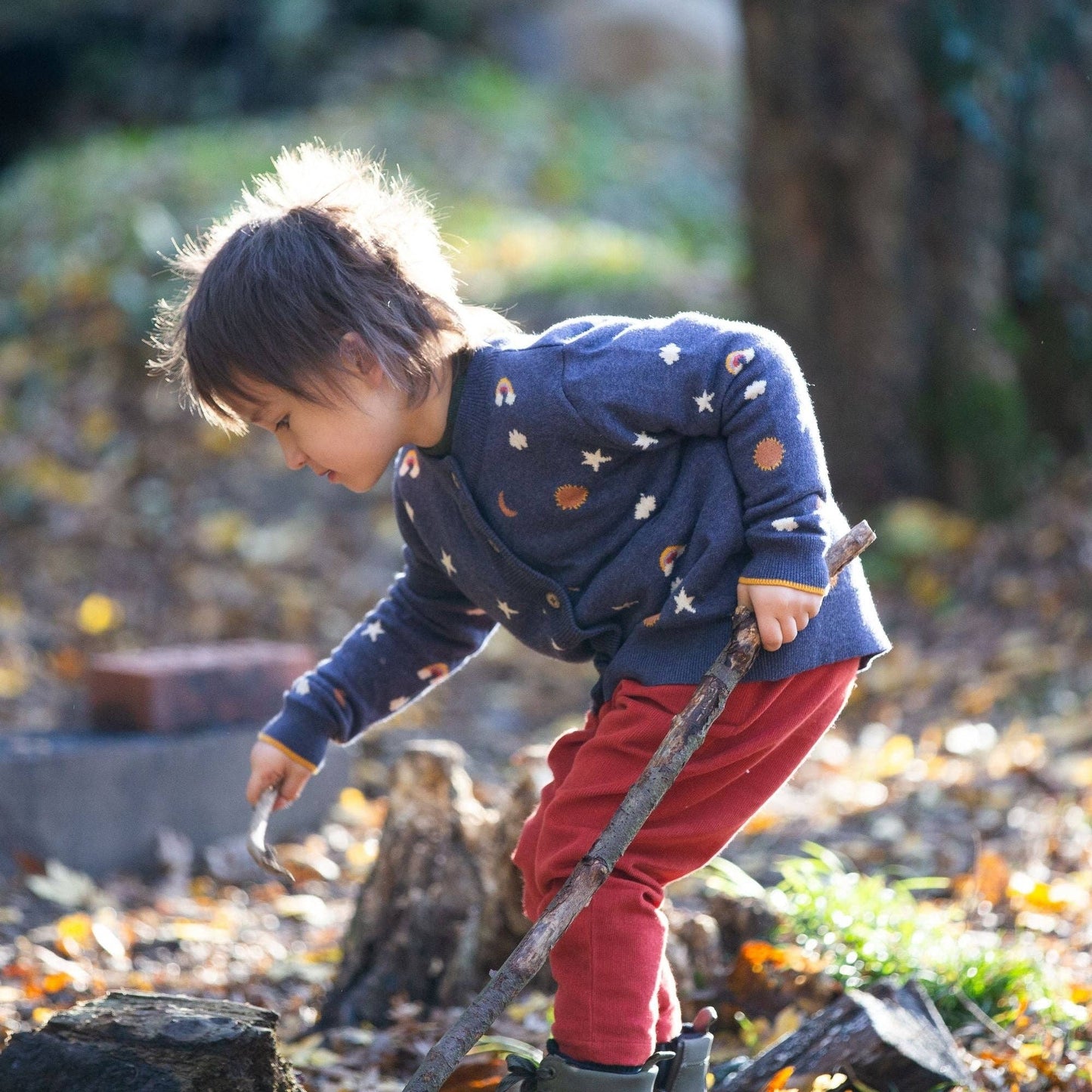 Child playing with sticks outside wearing around the sun knitted cardigan