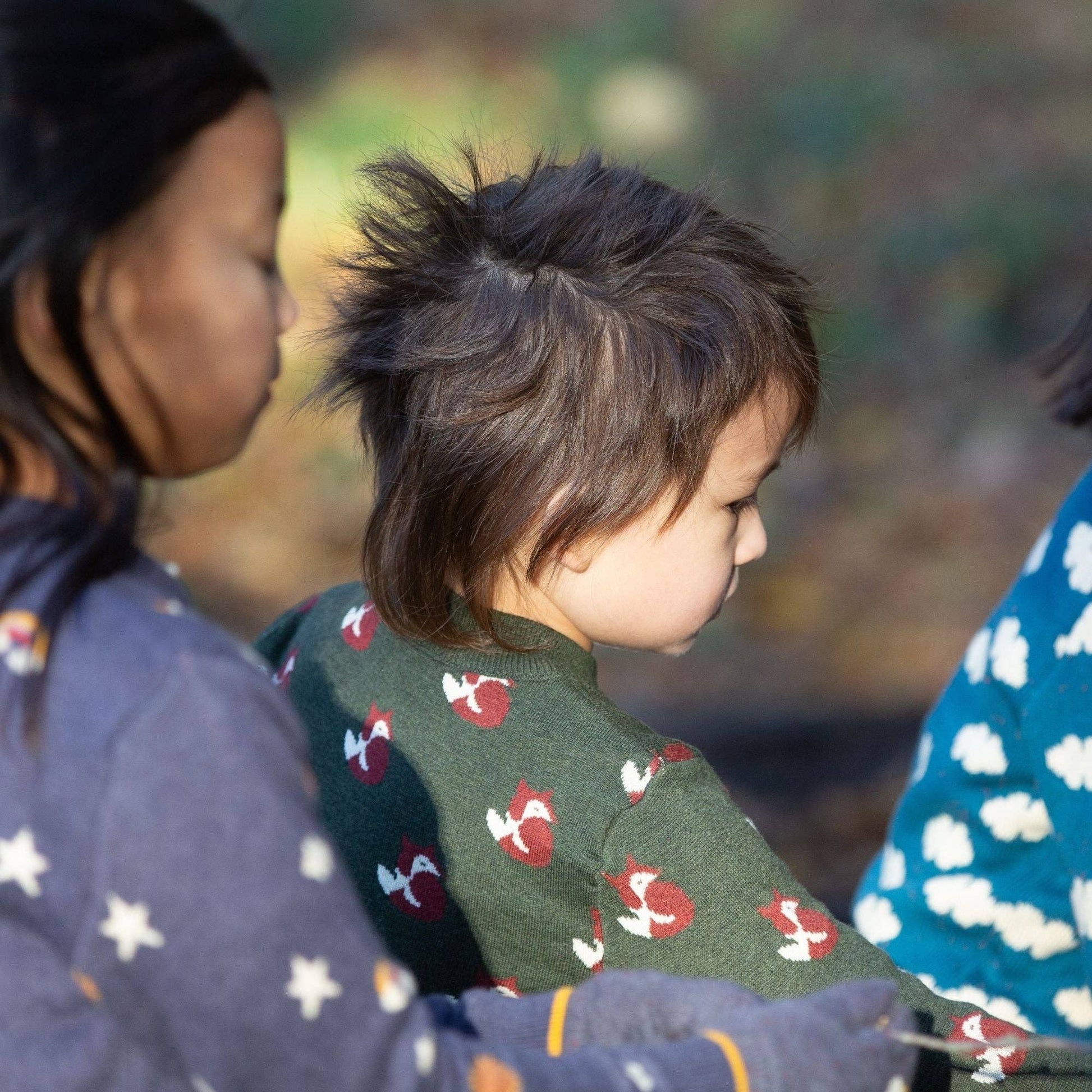 Children sitting in the woods wearing organic knitted sweaters by Little Green Radicals