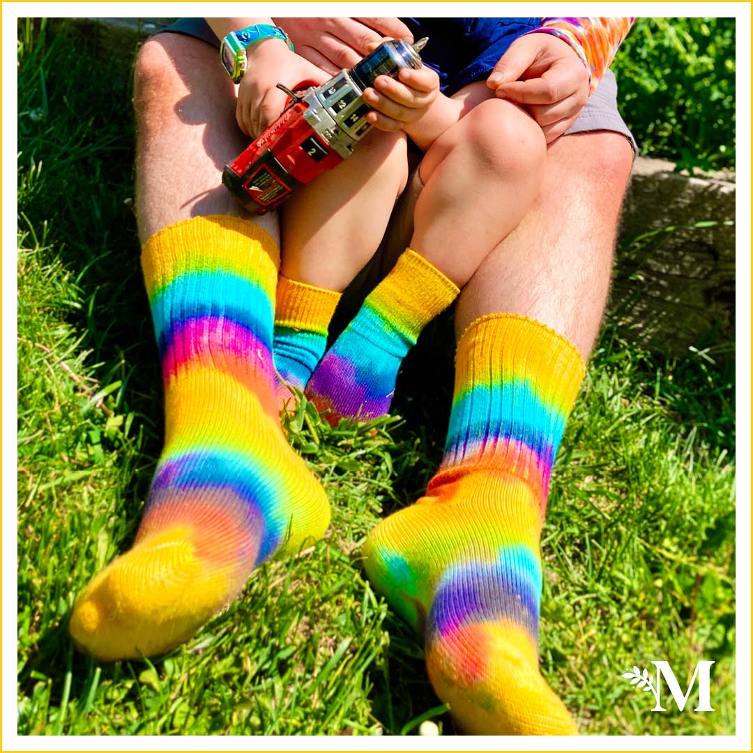 close-up shot of an adult and a toddler sitting on grass wearing tye-die organic socks