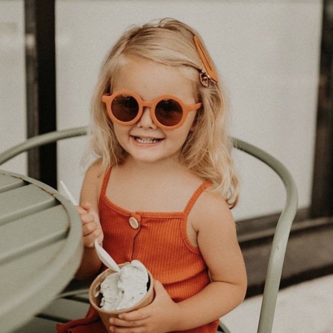 child sitting on a chair eating ice cream wearing orange eco sunglasses