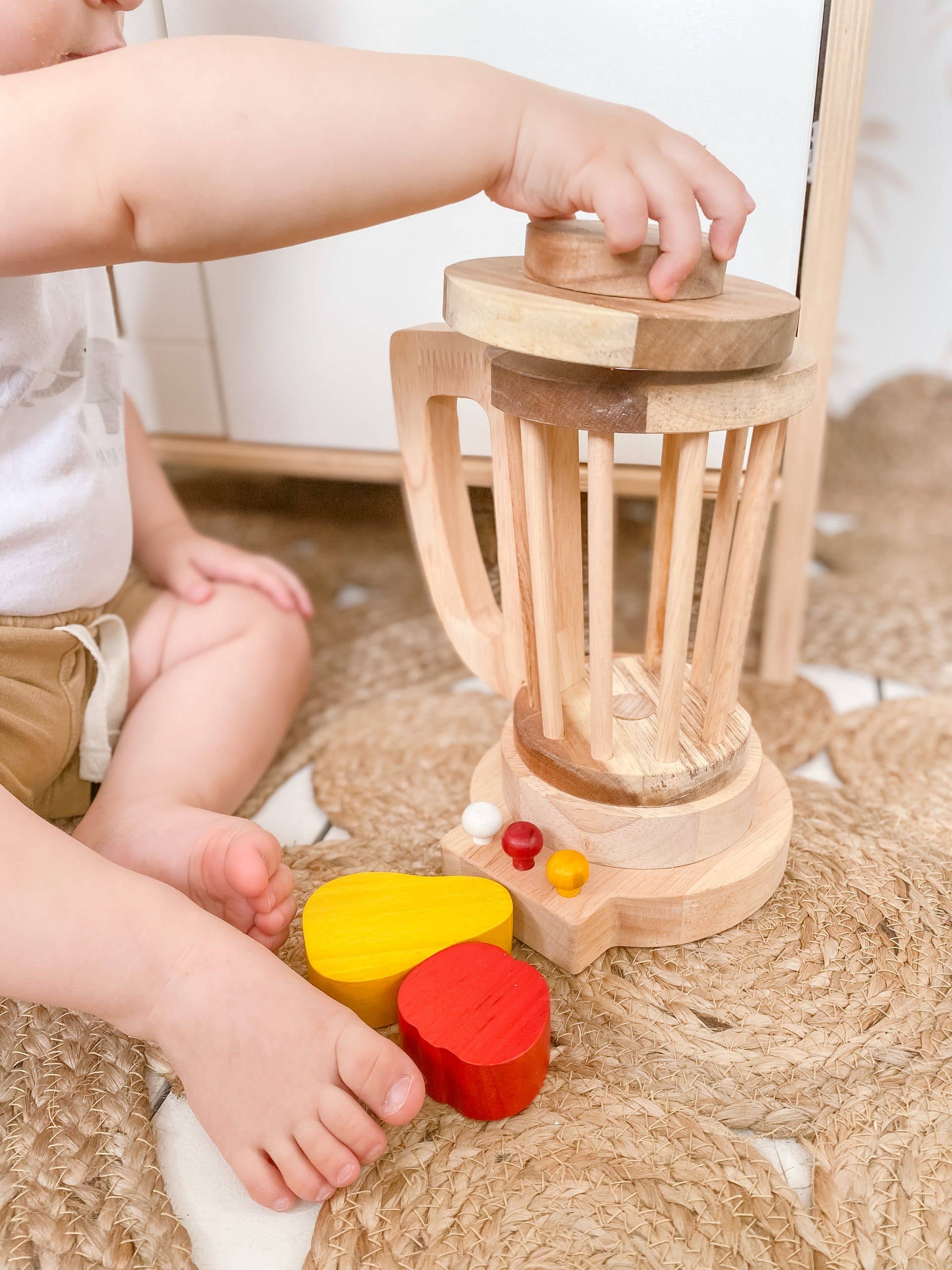 a baby sitting on the floor playing with a wooden blender by qtoys