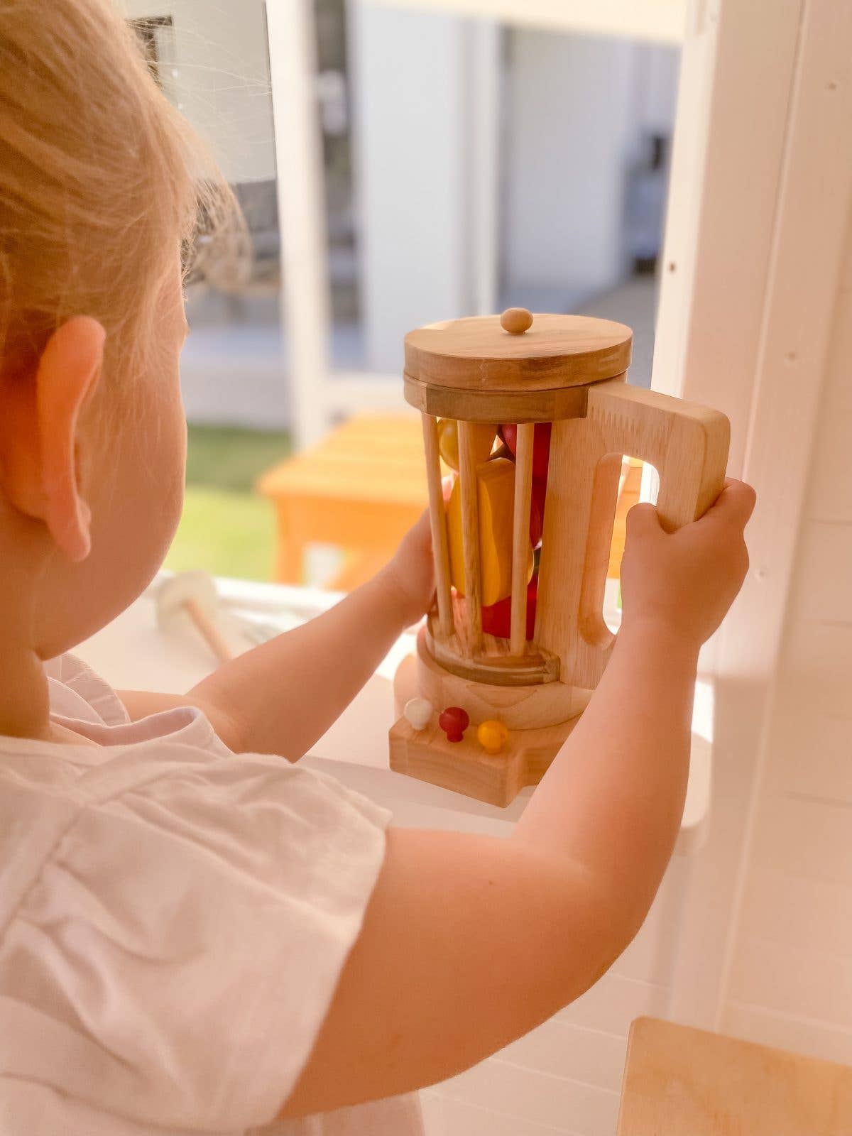 child standing in front of a window playing with a wooden blender