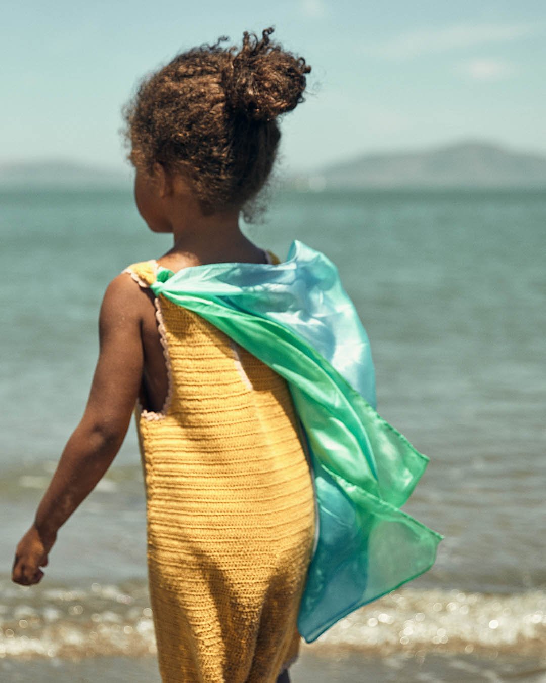 child standing on the beach wearing Sea mini play silk as a cape