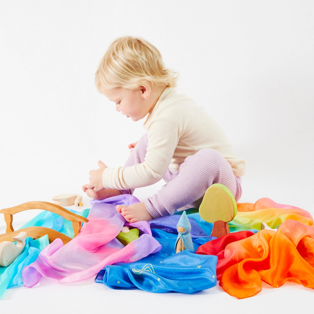 Child sitting on the floor playing with mini enchanted playsilks and wooden toys