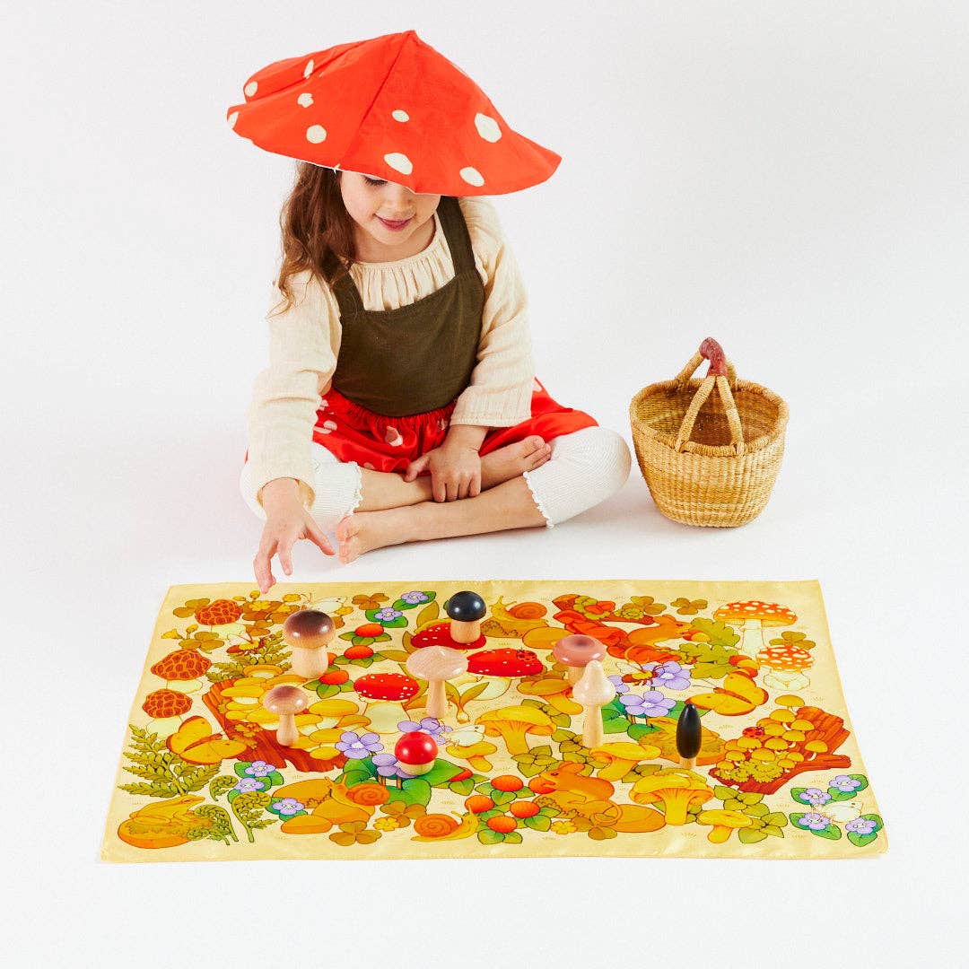 Child wearing a silk mushroom costume playing with wooden mushroom set on a mushroom playsilk