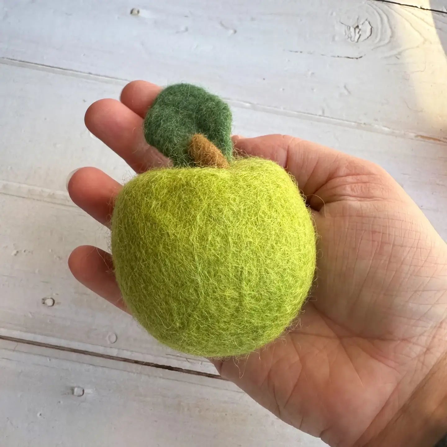 Hand holding a large felt green apple