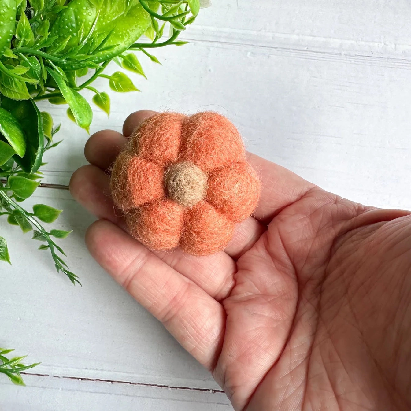 A hand holding a mini felt pink pumpkin