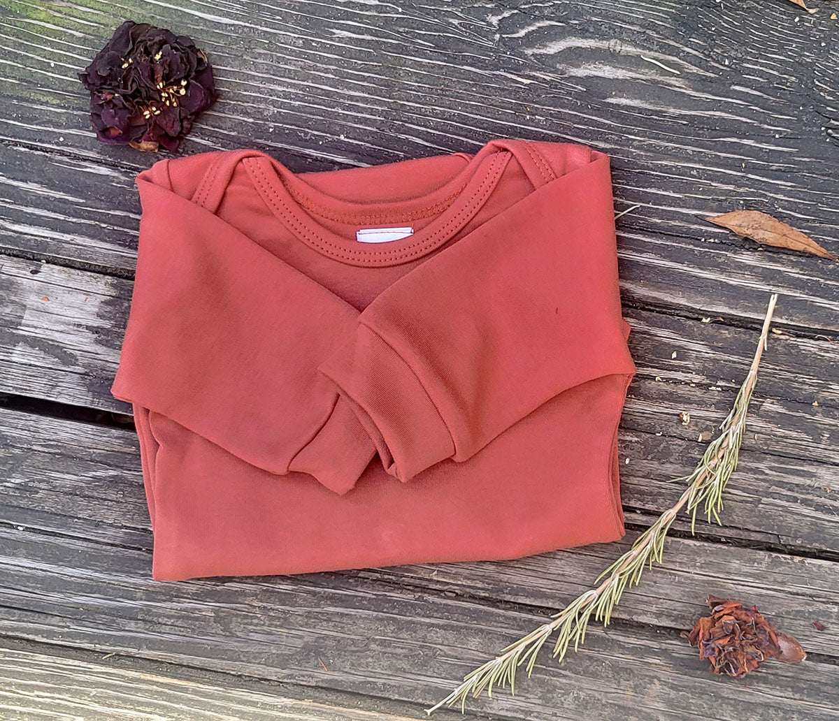 Terracotta Long Sleeve Onesie folded on a table