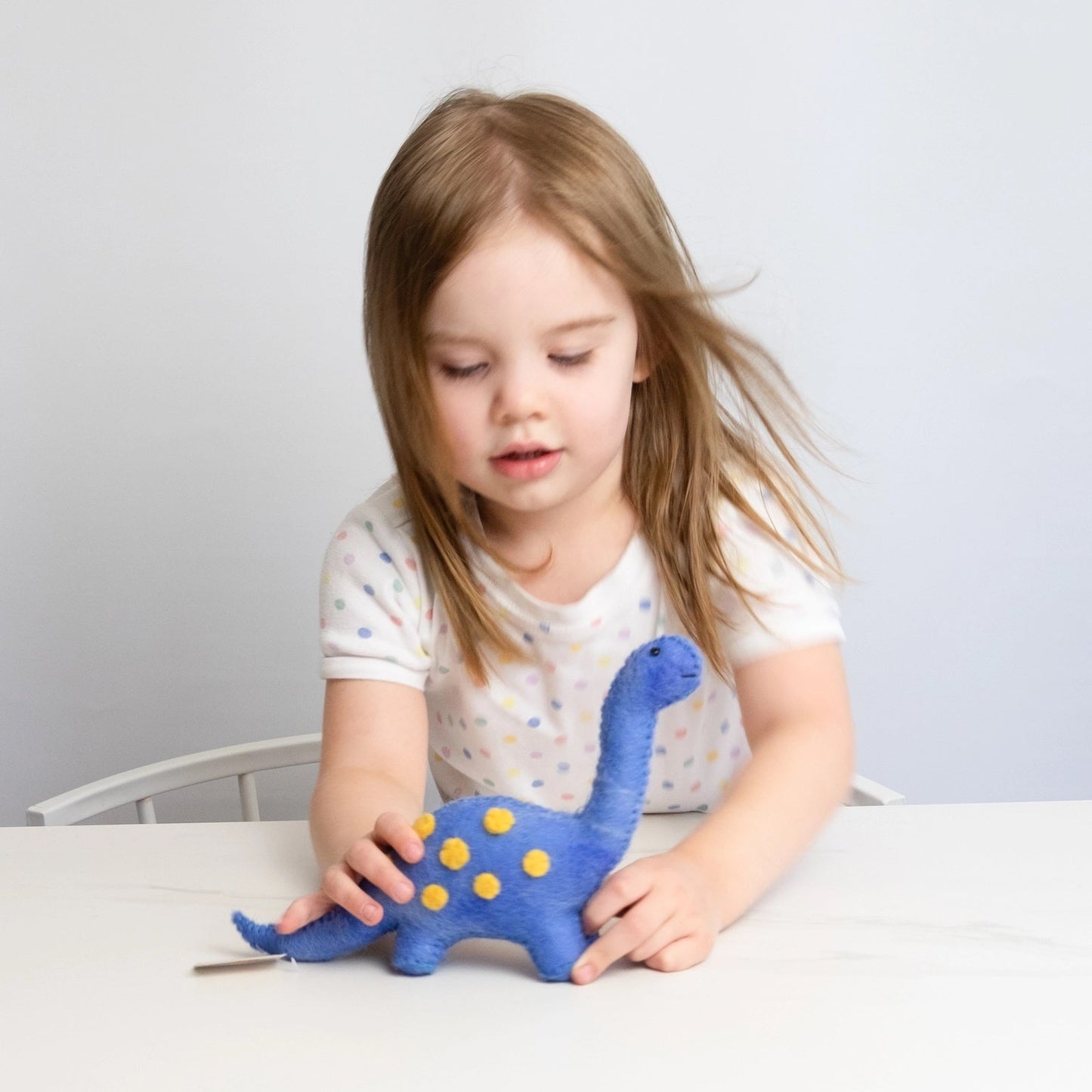 child playing with a blue mini dinosaur on a table