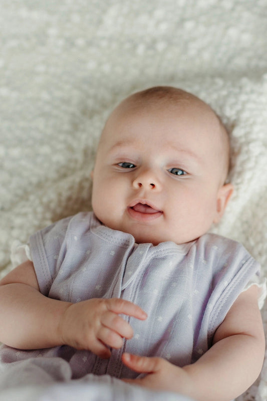 baby laying on a fuzzy blanket wearing a lavender stars muslin sleep sack